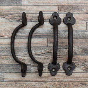 Può includere: Quattro maniglie per porte in metallo nero con un design decorativo. Le maniglie sono su uno sfondo di legno.