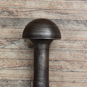 Op de afbeelding: Een donkerbruine flesstopper met een afgeronde bovenkant en een cilindrische steel. De stopper heeft een getextureerd oppervlak. De achtergrond is een houten oppervlak.