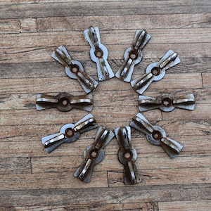 Op de afbeelding: Tien zilverkleurige metalen ladegrepen in de vorm van een strik. De grepen zijn in een cirkel op een houten oppervlak gerangschikt.