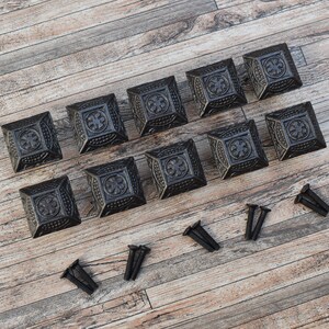 May include: Twelve black metal square cabinet knobs with ornate designs and a set of screws.
