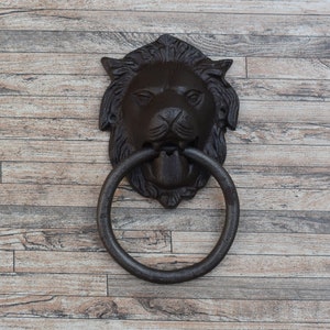 May include: A black cast iron door knocker shaped like a lion's head with a ring pull. The knocker is mounted on a wooden door.