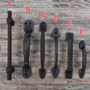 May include: Six different styles of black metal door handles. The handles are arranged in a row on a wooden background.