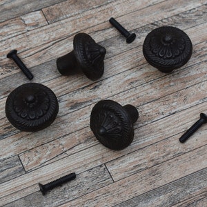 Può includere: Cinque pomelli per mobili in metallo nero con un design floreale decorativo. I pomelli hanno una base rotonda e un centro rialzato con una parte superiore appuntita.