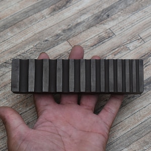 May include: A black metal tool with a series of parallel ridges. The tool is about 10 inches long and 1 inch wide.