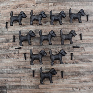 May include: Twelve black cast iron dog door pulls with screws. The dog pulls are arranged in a triangle shape on a wooden surface.