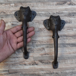 May include: Two black cast iron door handles shaped like elephant heads. The handles are about 15 inches long and have a detailed design.