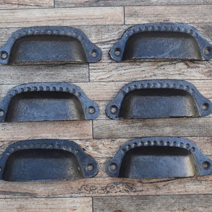 Op de afbeelding: Zes zwarte metalen ladegrepen met een decoratieve parelrand. De grepen zijn gerangschikt in twee rijen van drie op een houten oppervlak.