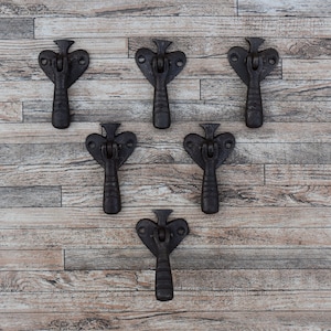 May include: Six black metal cabinet door pulls with a heart-shaped top and a lever handle. The pulls are arranged in a triangular pattern on a wooden background.