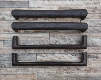 May include: Four black metal drawer pulls with a rounded rectangular shape. The pulls are arranged vertically on a wooden surface.