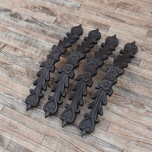 May include: Four black wooden decorative pieces with a floral design. The pieces are arranged in a row on a wooden surface.