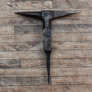 May include: A black metal anvil with a pointed tip and a flat top. The anvil is sitting on a wooden surface.