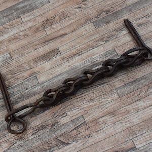 May include: A rusty metal chain with two hooks on the ends. The chain is lying on a wooden surface.