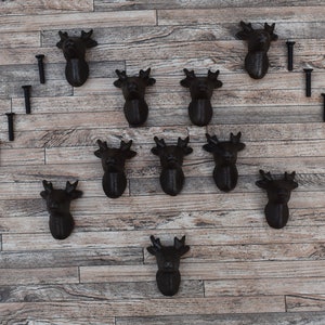 May include: A set of 11 black cast iron deer head hooks with screws. The hooks are arranged in a heart shape on a wooden background.
