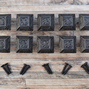 Könnte beinhalten: Zwölf schwarze quadratische Schrankknöpfe mit verzierten Designs und einem Satz Schrauben.