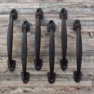 Puede incluir: Seis tiradores de puerta de color bronce oscuro sobre una superficie de madera marrón claro. Los tiradores tienen un diseño clásico y curvado con un acabado texturizado. Cada tirador mide unos 20 cm de largo, adecuados para armarios o puertas.