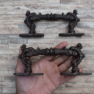 Op de afbeelding: Twee sierlijke gietijzeren deurgrepen met een decoratief scroll-ontwerp. De grepen zijn zwart en hebben een rustieke afwerking.
