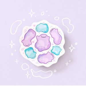 May include: A sticker featuring a cluster of cartoon-style blobs in shades of purple and teal, with small star details. The blobs have simple smiling faces. The background is a light purple with white doodle accents.