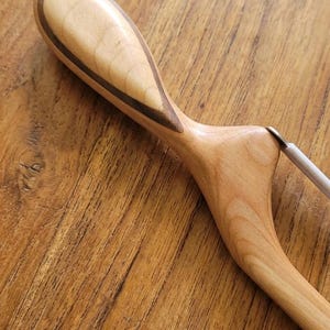 May include: A wooden clothes hanger with a light-colored, teardrop-shaped handle. The handle has a dark brown accent stripe. The hanger's body is a light brown color, and it has a metal hook.
