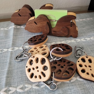 May include: A wooden dog-shaped business card holder in dark brown wood, holding a light green card with the text "les JOURS". Several circular wooden keychains with a perforated lotus root pattern in light and dark wood tones are attached to silver metal clips.