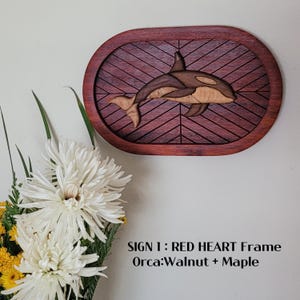 Könnte beinhalten: Wandkunst aus Holz mit einem Orca-Wal-Design. Der Orca ist aus Walnuss- und Ahornholz gefertigt und in einem roten Herzrahmen mit Fischgrätenmuster platziert. Das Schild ist an einer weißen Wand befestigt. Der Text auf dem Bild lautet "SIGN 1: RED HEART Frame Orca: Walnut + Maple."