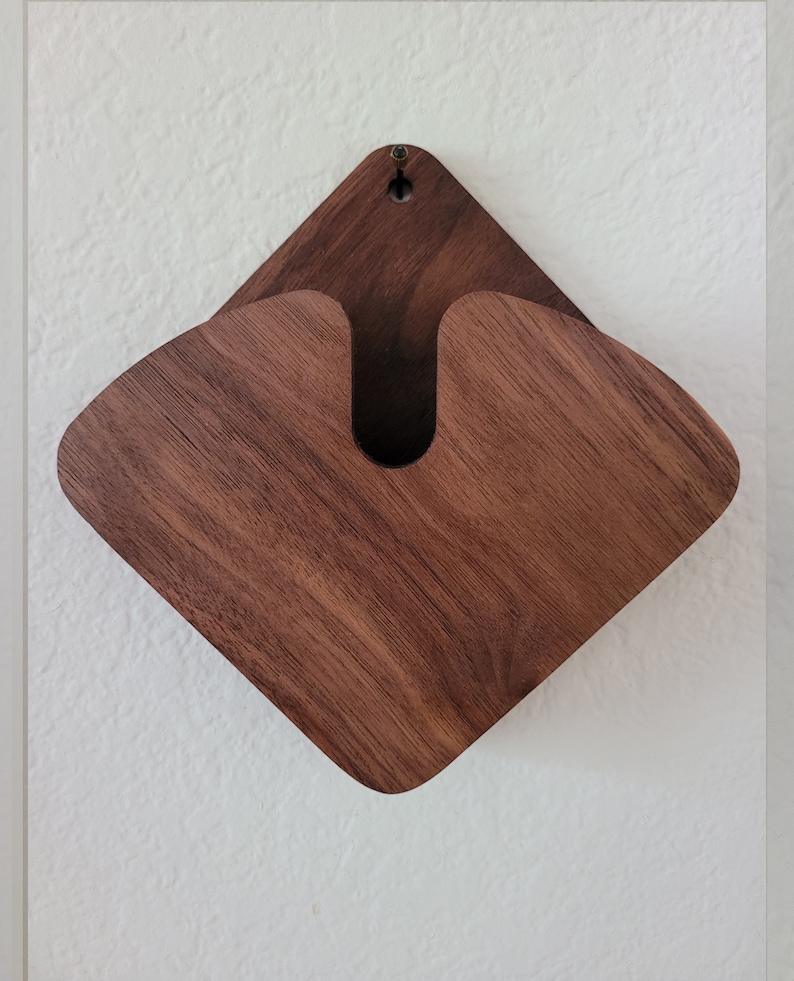 May include: A wall-mounted wooden organizer with a diamond-shaped design. The organizer is made of dark brown wood and features a curved opening in the center. A small hole is at the top for hanging. The wood grain is visible.
