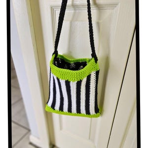 Puede incluir: Una bolsa de crochet a rayas blancas y negras con un ribete verde lima. La bolsa tiene un forro verde lima con un patr&oacute;n de calavera. La bolsa tiene una correa negra.