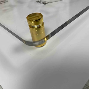 Pode incluir: Close-up de um suporte de metal dourado com base quadrada. O suporte &eacute; usado para exibir uma imagem ou uma obra de arte emoldurada.