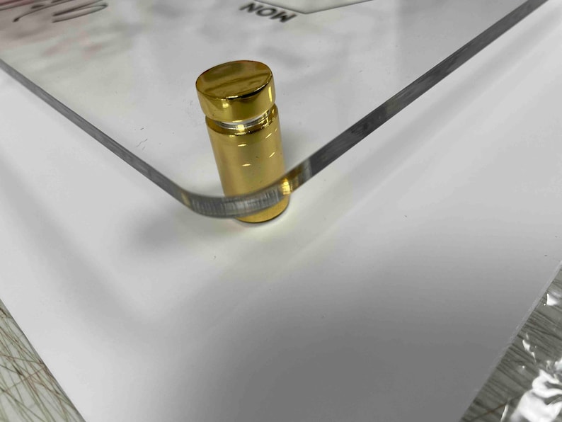 Pode incluir: Close-up de um suporte de metal dourado com base quadrada. O suporte &eacute; usado para exibir uma imagem ou uma obra de arte emoldurada.