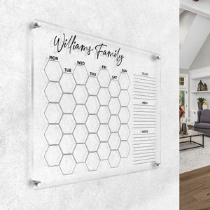 May include: A clear acrylic dry-erase calendar with a honeycomb grid design. The calendar is labelled with the days of the week: Monday, Tuesday, Wednesday, Thursday, Friday, Saturday, and Sunday. The calendar also has sections for "To Do", "Menu", and "Notes". The text "Williams Family" is written at the top of the calendar.