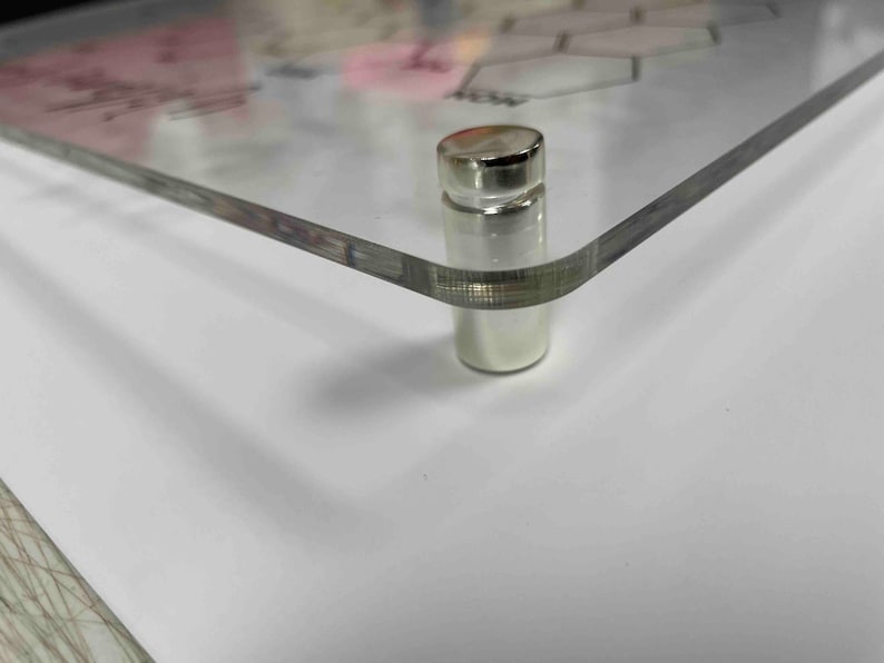 Pode incluir: Close-up de um suporte de metal prateado com uma parte superior lisa e arredondada. O suporte est&aacute; preso a uma superf&iacute;cie de acr&iacute;lico transparente.