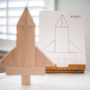 May include: A wooden rocket toy in front of a white easel with a drawing of a rocket labelled "ROCKET".