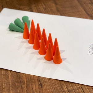 K&ouml;nnte beinhalten: Eine wei&szlig;e Tafel mit dem Wort "KAROTTE" darauf. Es sind neun orangefarbene Kegel in einer Reihe angeordnet, mit einer gr&uuml;nen Blattform an der Spitze der Reihe.