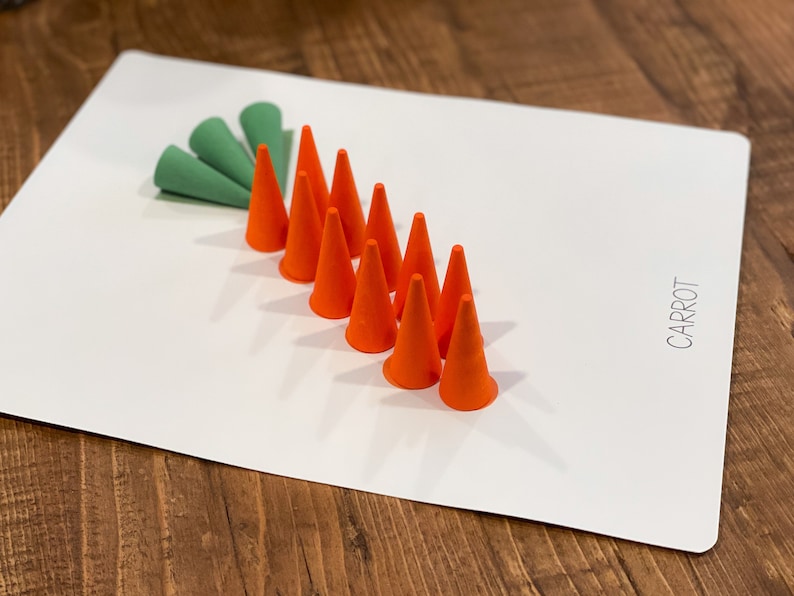 K&ouml;nnte beinhalten: Eine wei&szlig;e Tafel mit dem Wort "KAROTTE" darauf. Es sind neun orangefarbene Kegel in einer Reihe angeordnet, mit einer gr&uuml;nen Blattform an der Spitze der Reihe.