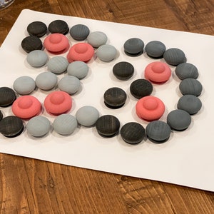 K&ouml;nnte beinhalten: Eine wei&szlig;e Tafel mit einem grauen, schwarzen und rosafarbenen Holzsteckpuzzle. Das Puzzle ist in Form eines Hasen und die Tafel sagt "BUNNY" in der rechten unteren Ecke.