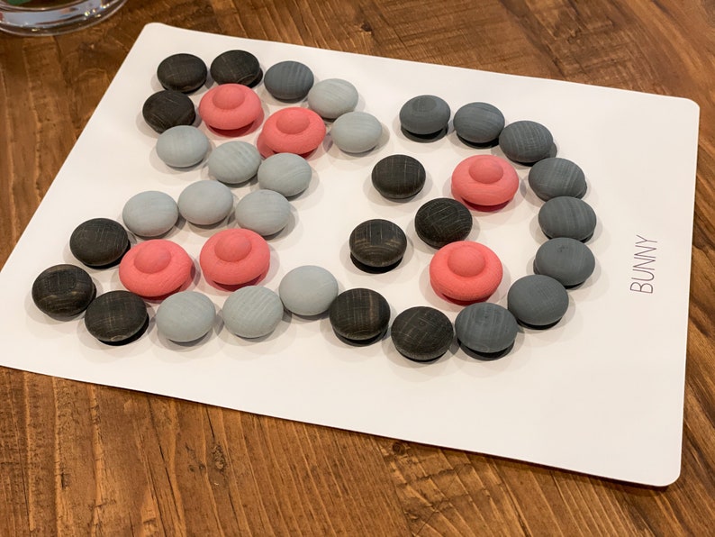 K&ouml;nnte beinhalten: Eine wei&szlig;e Tafel mit einem grauen, schwarzen und rosafarbenen Holzsteckpuzzle. Das Puzzle ist in Form eines Hasen und die Tafel sagt "BUNNY" in der rechten unteren Ecke.