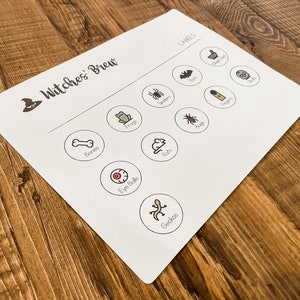 May include: A white game board with the title "Witches' Brew" and a witch's hat icon. The board has circles with various Halloween-themed images and labels, such as "Bones", "Eye Balls", "Frogs", "Rats", "Spiders", "Bugs", "Toads", "Fingers", "Bats", and "Geckos".