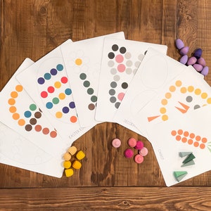 K&ouml;nnte beinhalten: Ein Satz von sieben druckbaren Osterei-Vorlagen mit verschiedenen Designs, darunter eine Karotte, eine Blume und ein verziertes Ei. Die Vorlagen sind von bunten Holzstiften und Kegeln umgeben.