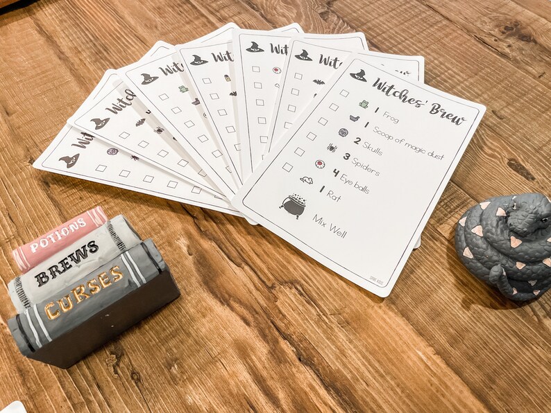 May include: A set of printable Halloween game cards with a witch's hat and the text "Witches' Brew". The cards have a checklist of ingredients for a witch's brew, including a frog, a scoop of magic dust, skulls, spiders, eyeballs, a rat, and instructions to mix well.