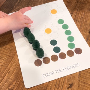 K&ouml;nnte beinhalten: Eine wei&szlig;e Karte mit dem Text "Color the Flowers" und zwei Blumenumrissen. Die Blumen bestehen aus wei&szlig;en Kreisen mit gelben Zentren. Die Karte ist von gr&uuml;nen und braunen Kreisen umgeben.