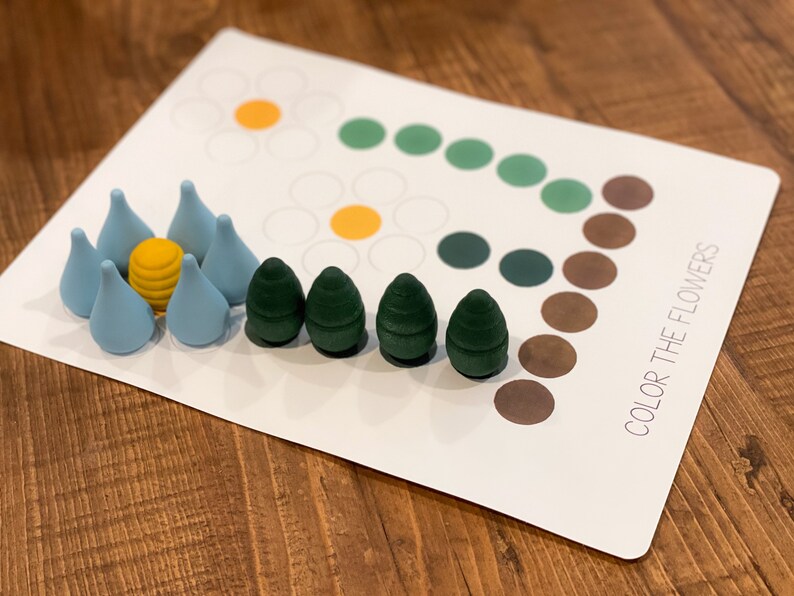 K&ouml;nnte beinhalten: Eine wei&szlig;e Karte mit dem Text "COLOR THE FLOWERS" darauf gedruckt. Die Karte hat ein Blumenmuster mit Kreisen in verschiedenen Farben. Es gibt kleine Holzst&uuml;cke in Blau, Gr&uuml;n und Gelb.