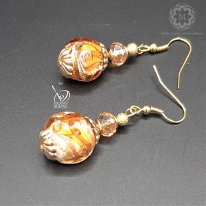 Peut inclure: Une paire de boucles d'oreilles en or avec des perles en verre ambre. Les perles ont un motif en spirale et des accents dorés. Les boucles d'oreilles ont une fermeture à crochet.