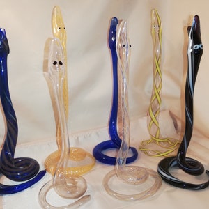Könnte beinhalten: Sechs Glasschlangen-Skulpturen in verschiedenen Farben und Mustern. Die Schlangen sind aufgerollt und haben ein realistisches Aussehen. Die Farben umfassen Blau, Gelb, Klar und Schwarz.