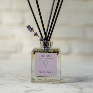 Könnte beinhalten: Eine klare Glasflasche mit schwarzen Diffusorstäbchen und einem Lavendelzweig. Die Flasche hat ein Etikett mit der Aufschrift "THE NINE BEAUTY & HOME SPA" und "TRUE STORY".