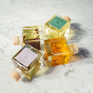 Könnte beinhalten: Vier Glasflaschen mit Korkstopfen, gefüllt mit einer gelben Flüssigkeit und kleinen Stücken getrockneter Blumen und Kräutern. Die Flaschen sind mit dem Text "THE NINE", "TRUE STORY", "WILD STORY" und "THE NINE" beschriftet.