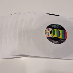 May include: A collection of multiple 7-inch vinyl records housed in white paper sleeves. The top record features a black Decca label with a colorful rainbow graphic, displaying the text "What You Gonna Do, Leroy?" and "Burl Ives" in white.