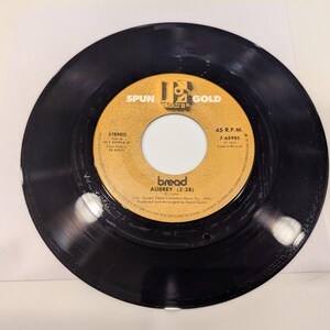 May include: A black vinyl record with a gold and white label. The label reads "Spun Gold" and features the band name "Bread" and the song title "Audrey". The record is a 45 RPM single.