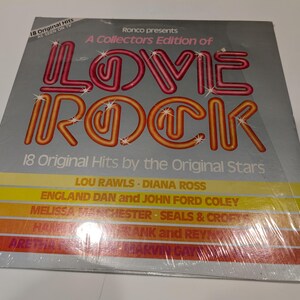 May include: A vintage vinyl record album titled "Love Rock." The album cover is silver with the words "LOVE ROCK" in a neon-style font. The album features 18 original hits by various artists, including Lou Rawls and Diana Ross.
