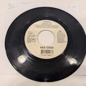 May include: A black vinyl record with the title "Alone" by the Bee Gees. The record is on a white paper sleeve. The label includes the text "Side A" and a barcode.