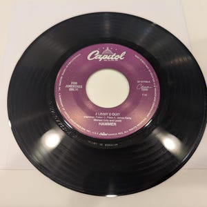 May include: A black vinyl record with a purple and white label. The label reads "2 Legit 2 Quit" by Hammer, with the Capitol Records logo. The record is in a clear plastic sleeve, suitable for music collectors.