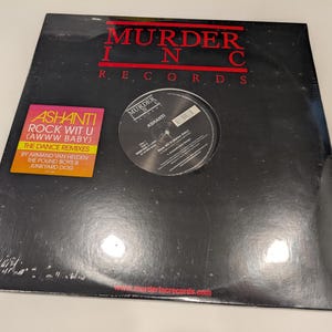 May include: A black vinyl record with a white label. The label has the text "MURDER INC RECORDS" in red and white. The record is titled "ASHANTI ROCK WIT U (AWWW BABY) THE DANCE REMIXES" in yellow and orange text. The record is by Armand Van Helden, The Pound Boys & Junkyard Dog.